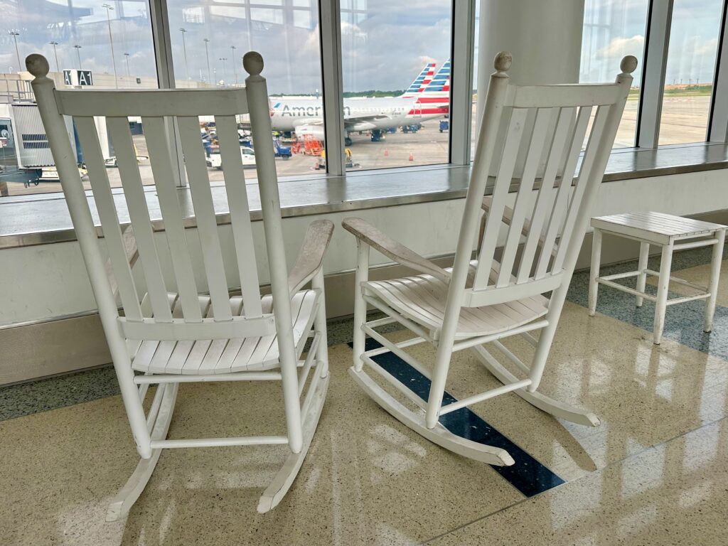 Two white rocking chairs in front of a window at Charlotte airport.
