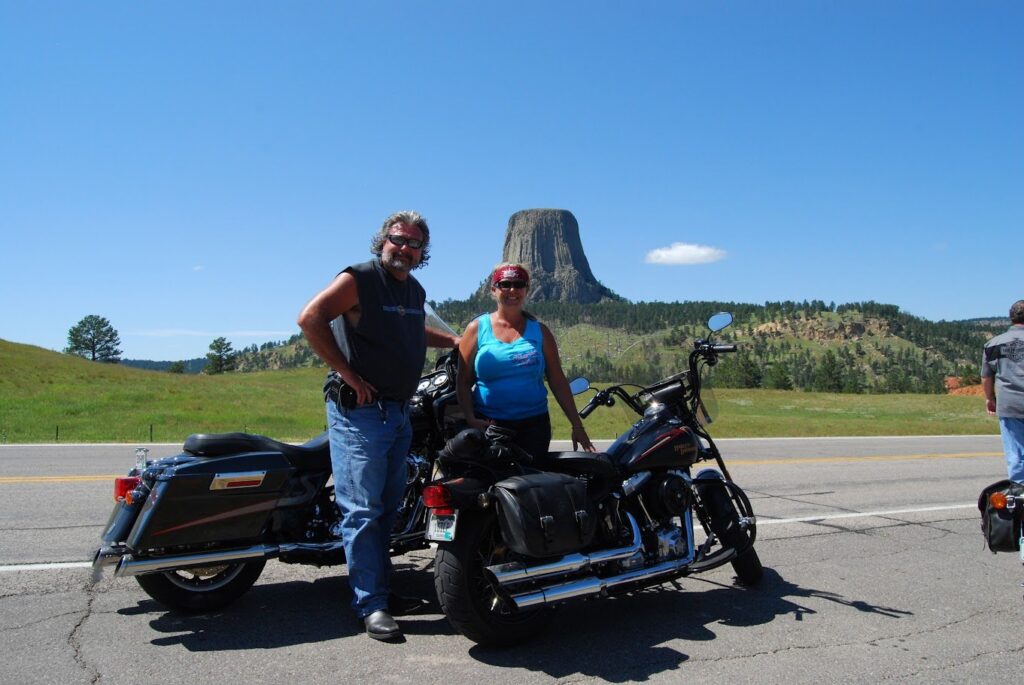 Man and woman pose with their Harleys in front of Devils Tower in South Dakota