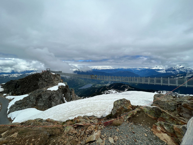 Swing bridge across a canyon. Views of mountains and snow patches