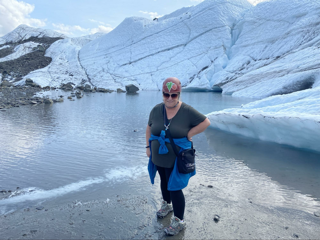 Women in hiking boots on a glacier in Alaska with melting water behind her.