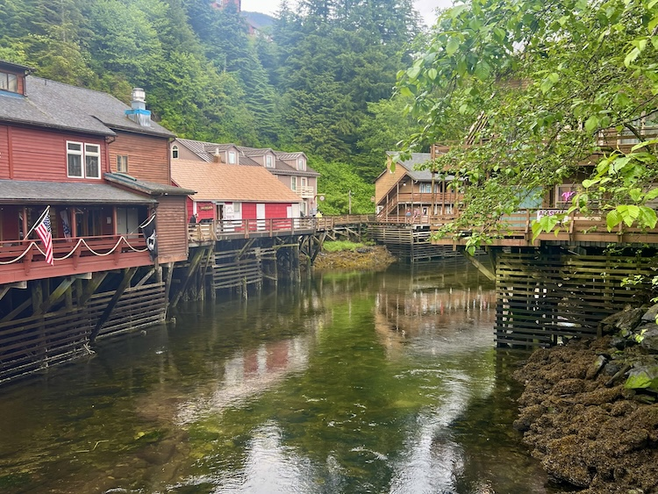 Colorful houses along a boardwalk above a river with green trees.