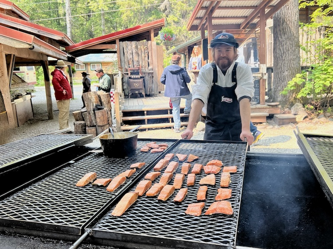 Cook preparing salmon over grill at an Old Miners Camp