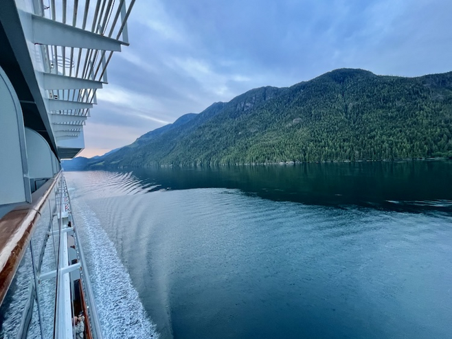 Side of Cruise ship with calm waters and forested Inside Passage land.