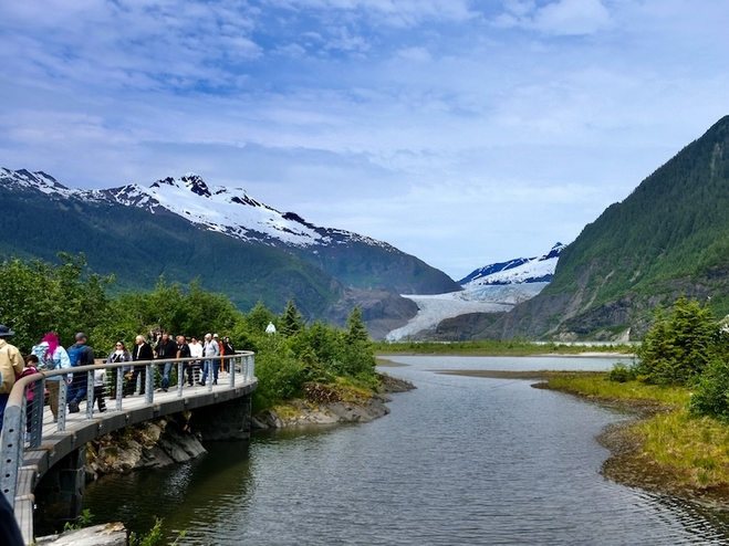 Mendenhall Glacier surrounded by mountains with people walking on a boardwalk above a stream.