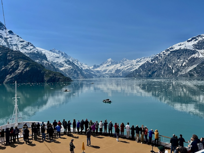 Still waters in front of Margerie Glacier while passengers line the bow of the ship