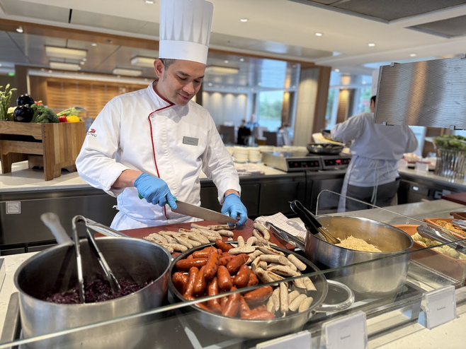 A chef in a white hat cuts sausages