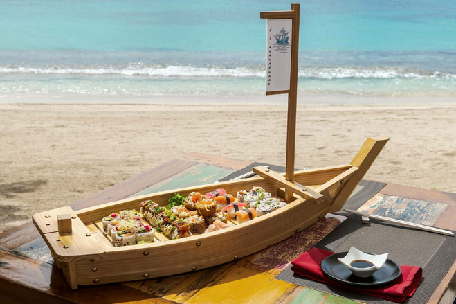 Wooden sailboat dish full of sushi on a beach