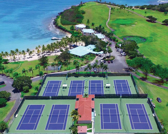 Arial view of blue tennis courts located near a beach with turquoise waters.
