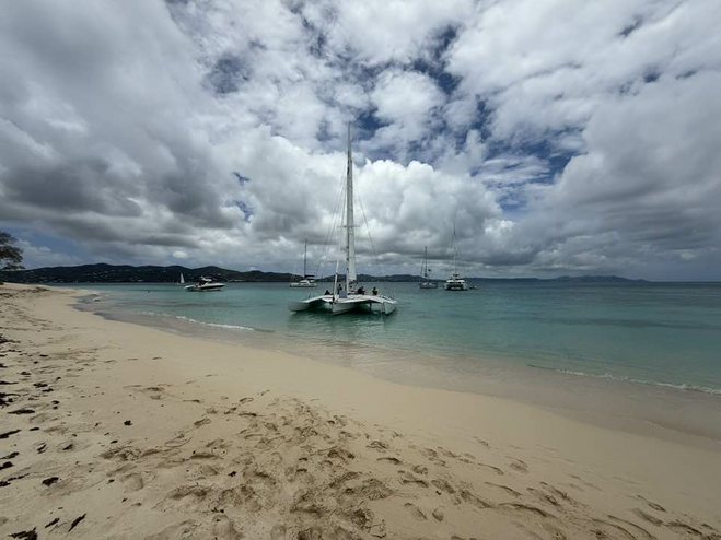 Catamaran sailboat on calm seas with clouds in the sky above and golden beach sand