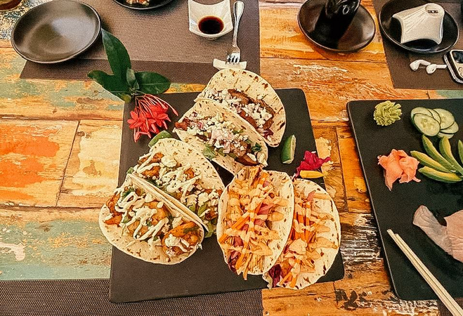 Six tacos on a rustic, painted table.