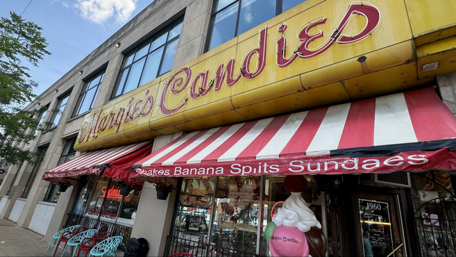 A yellow sign with LED letters spelling Margie's Candies above a red and white striped awning. 