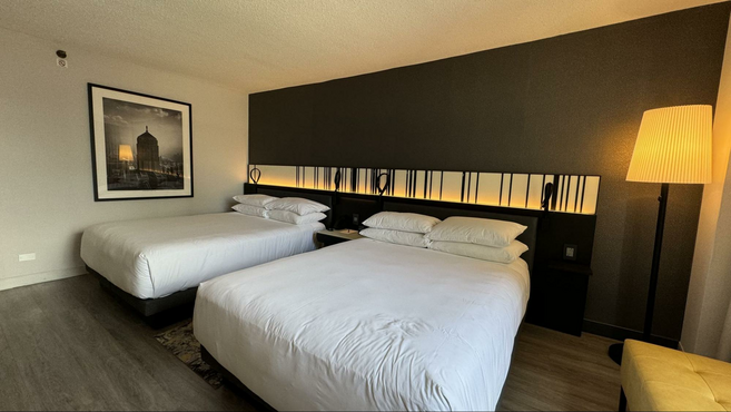 Two beds in a hotel room with a lamp, black wall and decorative art work on the wall. 