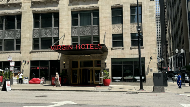 Red lettering of the Virgin Hotels logo on the corner of a metropolitan block. 