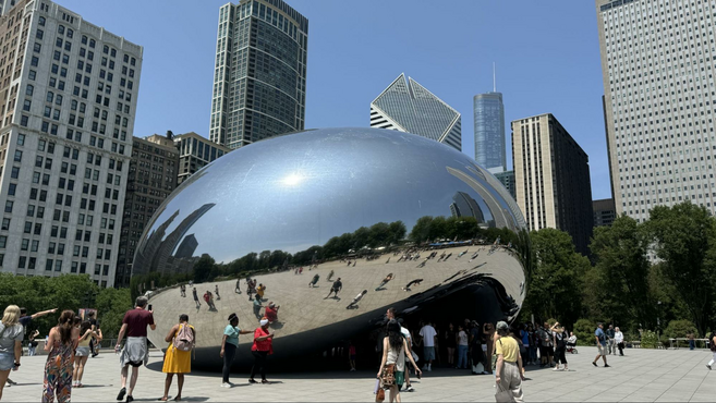 Large reflective metallic bean-shaped structure in front of skyscrapers.