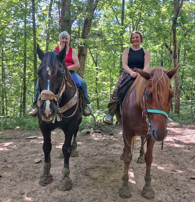 Two women on horses in woods.