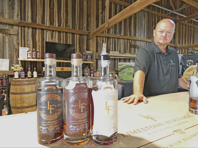 A man in barn with three whiskey bottles on table.