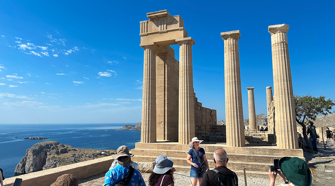Tourists at the Acropolis of Lindos with view of the Aegean see in the background.