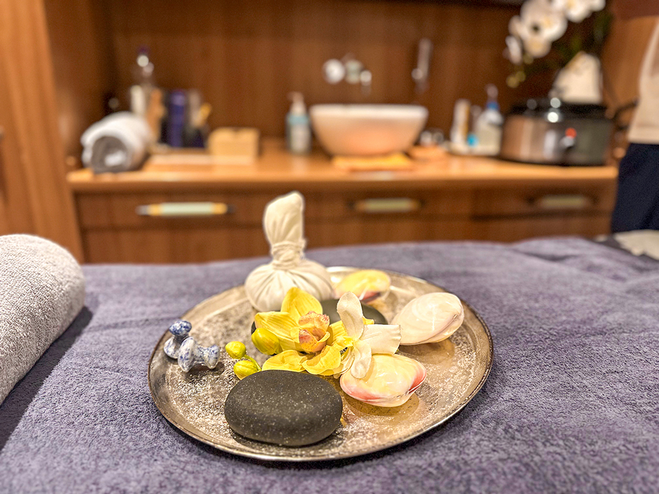 A plate of hot stones with seashells and flowers on a massage table