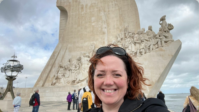 A smiling woman in front of the Monument to the Discoveries in Lisbon, Portugal