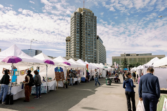 Open-air market with white tents and vendors selling products 