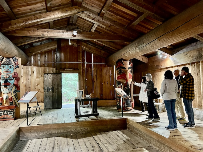 Interior of a Native Clan House with visitors viewing a carved totem in Anchorage.