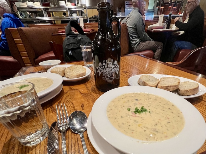 Bowls of seafood chowder on the wood table with bread and cutlery. 