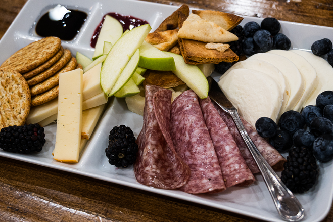Salami, assorted cheeses, fruits and crackers on a white dish