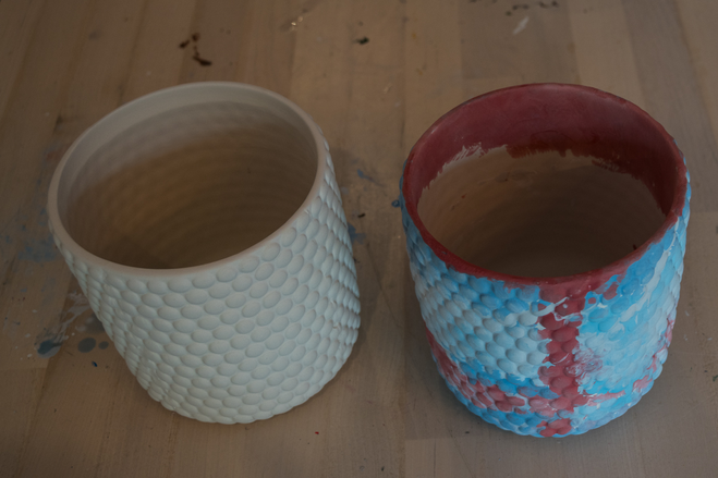 A plain white clay pot and a painted pot in shades of blue and red
