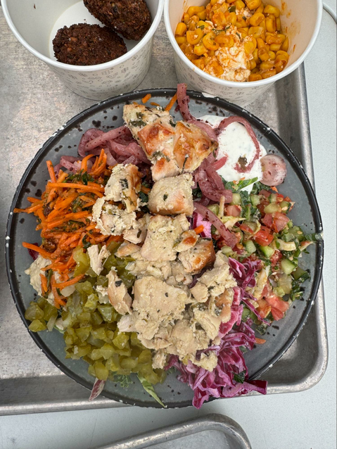 A mediterranean salad with slaw, chicken, and mezze dips from Yafo Kitchen