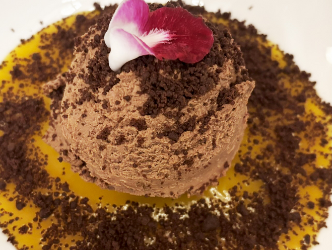 A large scoop of dark chocolate mouse on top of passion fruit gel. All of it is springled with cocoa 