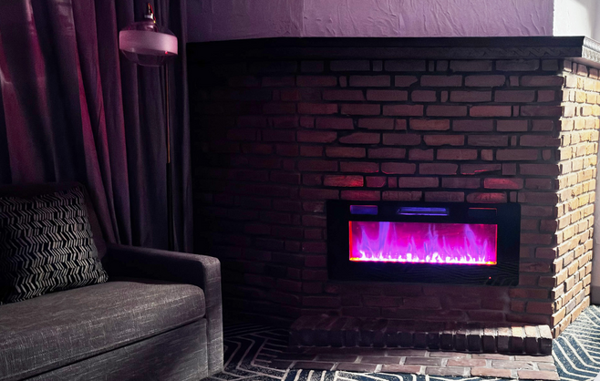 A coach next to a gas fireplace with pink and purple light. 