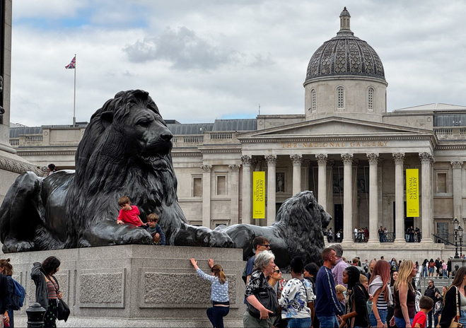 Lion at the base of Nelson's Column in Trafalgar Square. The National Gallery of Art in the background.