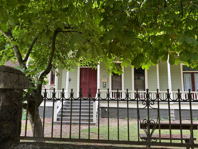 Green Queen Anne style home with wrap around porch and wrought iron decorative fence.