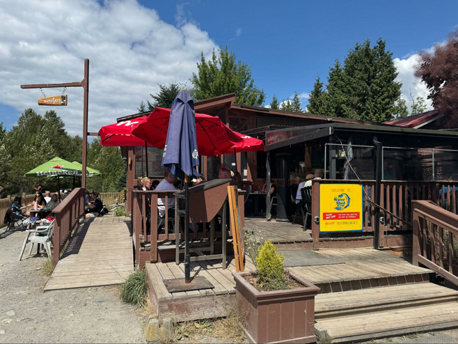 Shack looking building with out door deck with seating overlooking a river.