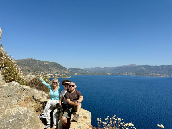 Family sitting on low wall overlooking Aegean coastline.