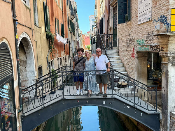 Family standing on narrow bridge over Venice canal.