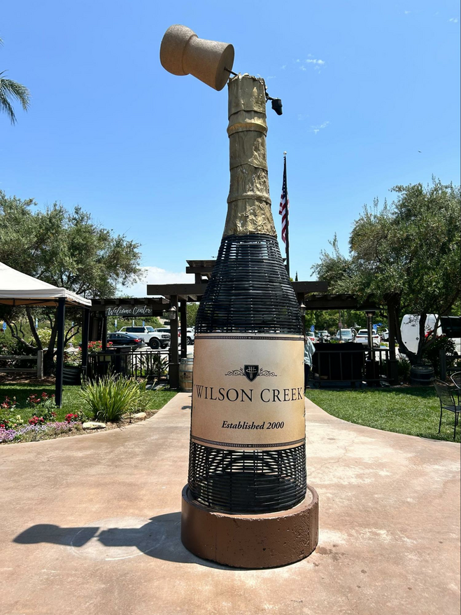 Art Installation of a lifesize bottle of Wilson Creek wine, parking lot of the winery in the background