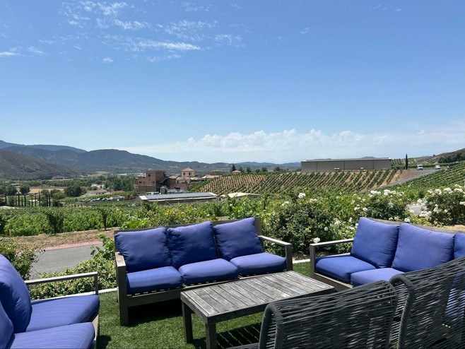 Sofas and lounge chairs sit out on the lawn of the Altisima winery, with green gardens and rolling vineyards in the background
