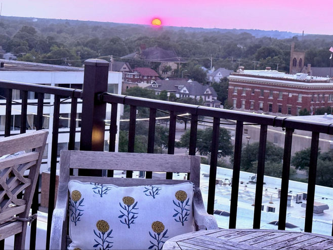 Sultry sunset colors of mauve with an orange setting sun in the distance give an ethereal feel to the Hotel Elkhart rooftop patio. Downtown buildings fill the vista until a thick line of trees begin to block the sun.