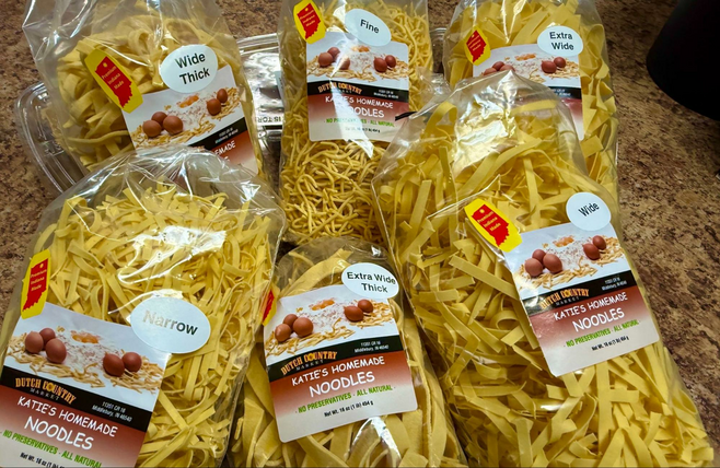 Katie's Homemade Noodles stickers fill the center front of six plastic bags. Smaller oval stickers declare the noodle size: wide, narrow, extra wide thick, fine, wide thick and extra wide.