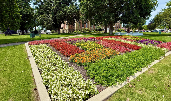 Horizontal blocks of flowers are planted densely to make an enormous square. White flowers border two sides, green a third and light red the fourth. In their middle are horizontals and squares of orange, yellow and darker red blooms, plus a hint of purple.