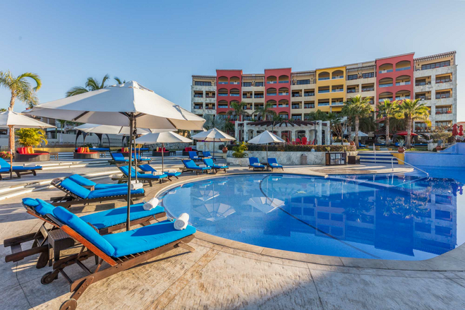 Red and yellow resort with blue pool and lounge chairs at Hacienda Encantada Los Cabos family resort