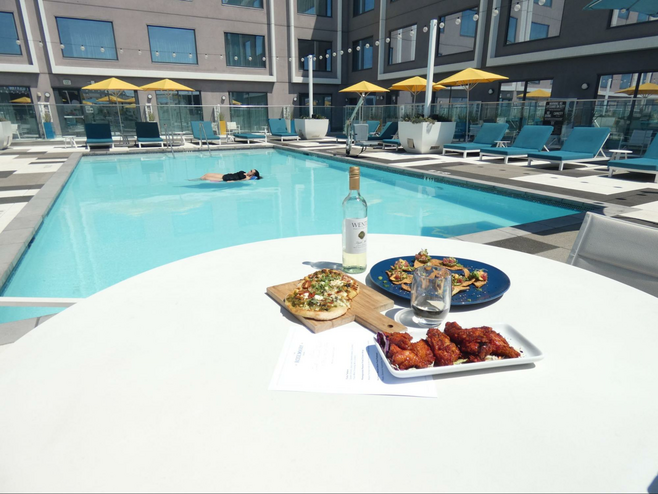 Three dishes of food and wine on table in front of pool.