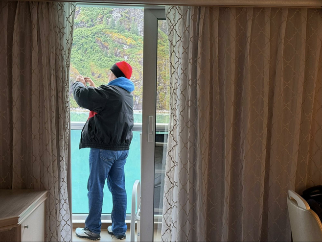 Man in a black jacket taking pictures on a cruise ship balcony in Alaska