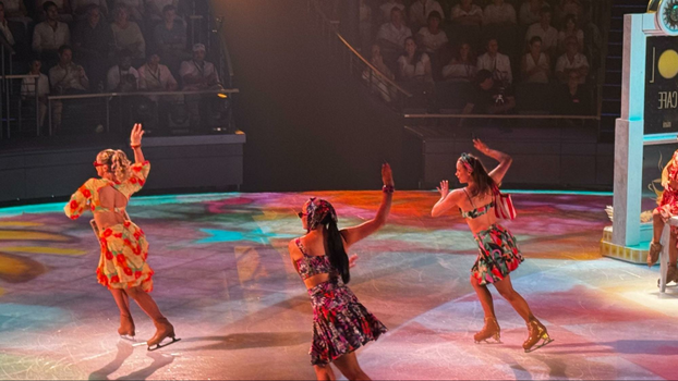 three ice skaters in floral skirt sets with their hands in the air gliding across the ice 