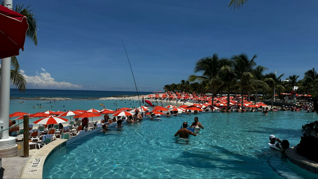 blue water splash pad with a man on a red boogie board next to two employees.