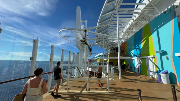 Man in a neon yellow jumpsuit ziplining over the ships edge.