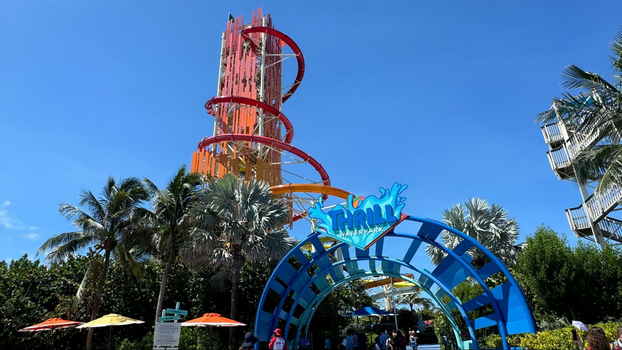 Crystal clear pool area with four people and a bunch of orange and white umbrellas in the sand.
