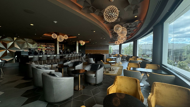 Interior seating area with yellow and silver lounge chairs, geodesic tiles and geometric lighting fixtures next to window panels.