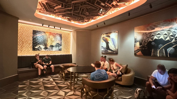 Dimly lit waiting area with people sitting on the chairs in front of pictures of Spaceship Earth